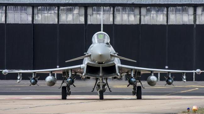 Rollender Eurofighter mit Bewaffnung vor Hangar.
