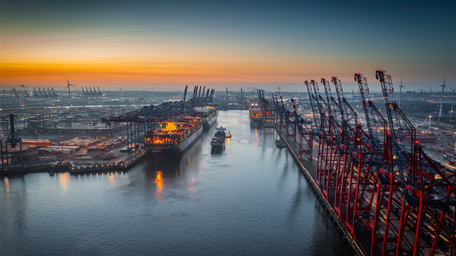 Auf dem Bild ist ein großer Hafen mit Frachtschiff auf dem Meer zu sehen. Im Hintergrund sieht man Windkraftanlagen. Auf dem Bild ist ein großer Hafen mit Frachtschiff auf dem Meer zu sehen. Im Hintergrund sieht man Windkraftanlagen.