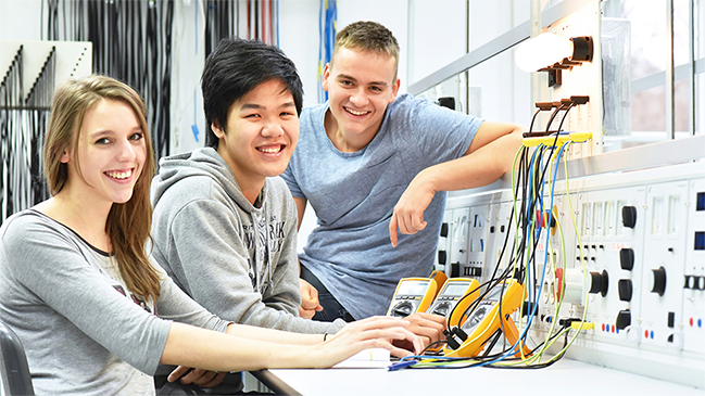 Drei Auszubildendeam Arbeitsplatz mit Elektrogeräten Drei Auszubildendeam Arbeitsplatz mit Elektrogeräten